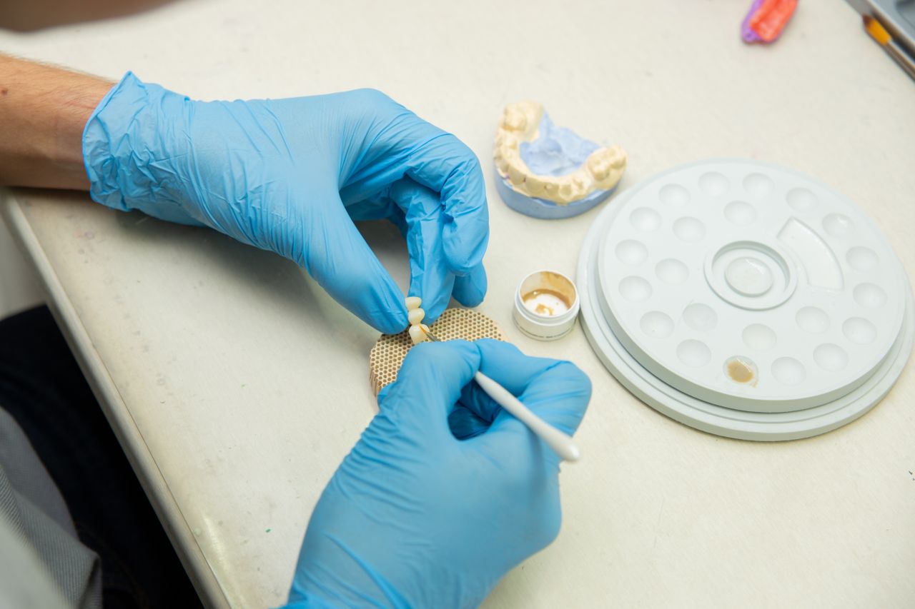 From above of crop anonymous orthodontist in latex gloves making fake teeth for denture in modern dental clinic